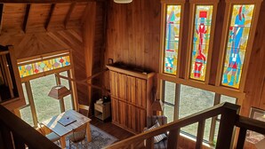 A wooden interior with a dining area, a staircase, and large stained glass windows.