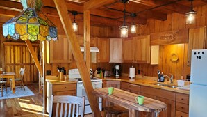 A wooden kitchen with a central island, wooden cabinets, and a hanging light fixture.