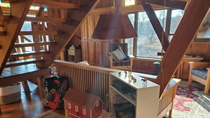 A wooden interior with a staircase, a small red house model, and a bookshelf with various items.
