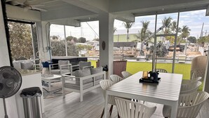 A spacious outdoor seating area with a table and chairs, a fan, and a trash bin.