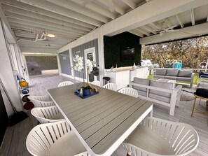Un patio techado con mesa, sillas, un sofá y zona de barbacoa.