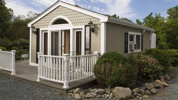 Ein eingeschossiges Haus mit Veranda, einer kleinen Terrasse und einem Kiesweg, der zum Eingang führt.