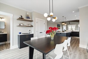 Una cocina moderna con armarios oscuros, una isla central y una zona de comedor con una mesa oscura y sillas blancas.