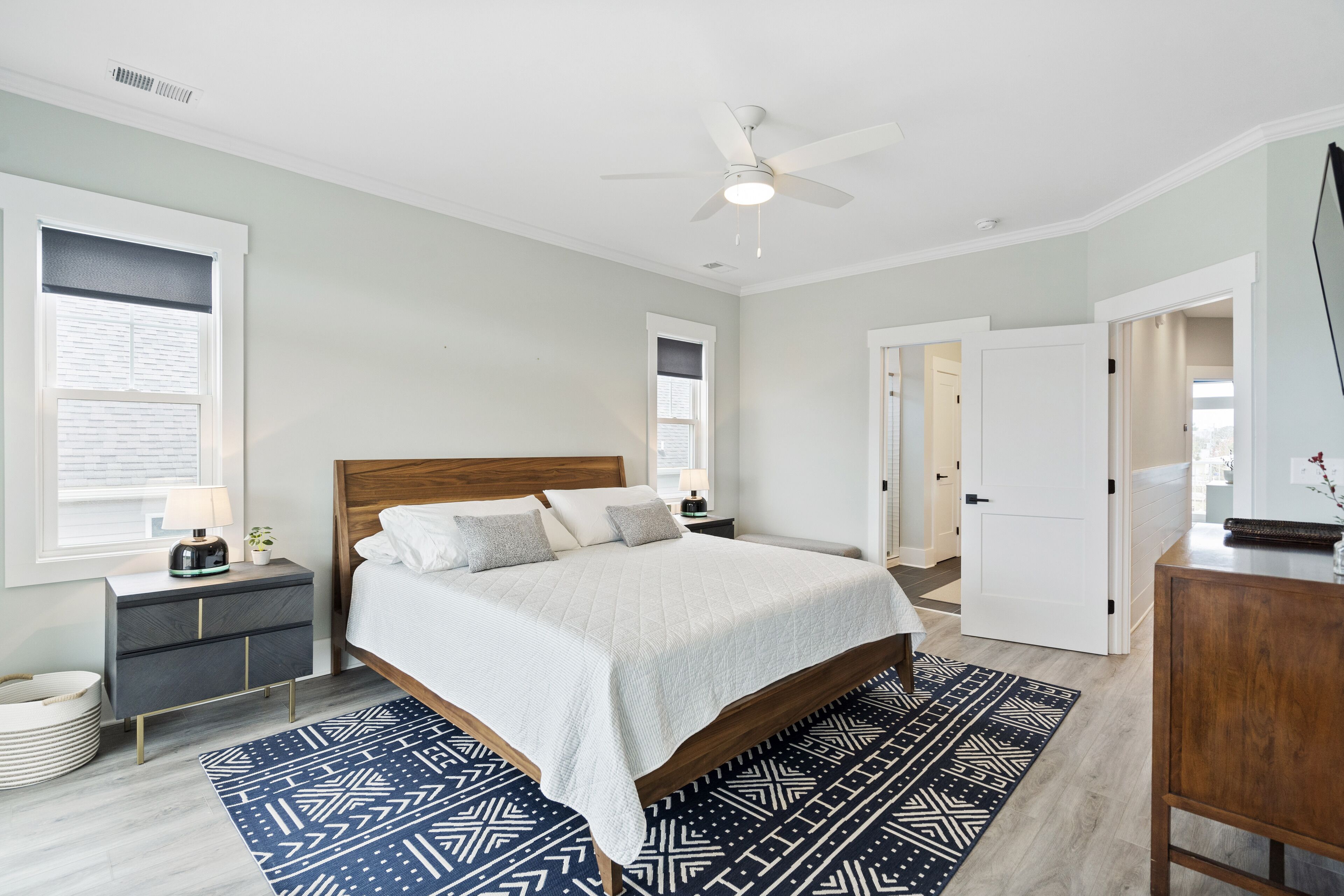 Quarto com cama, mesas de cabeceira, ventilador de teto e tapete estampado.