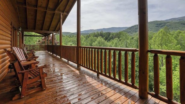A wooden deck with chairs, a covered area, and a view of a forested mountain range.