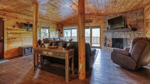 A cozy cabin interior with wooden walls, a stone fireplace, a comfortable sofa, and a recliner.