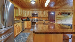 A wooden cabin-style kitchen with a large island, stainless steel appliances, and a welcome sign.