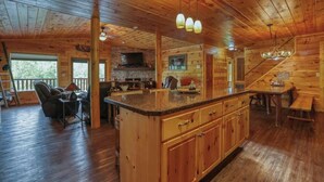A wooden cabin interior with a large kitchen island, dining area, and a fireplace.