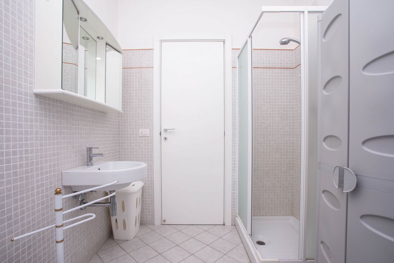 Un bagno moderno con lavandino, specchio e doccia bianchi.