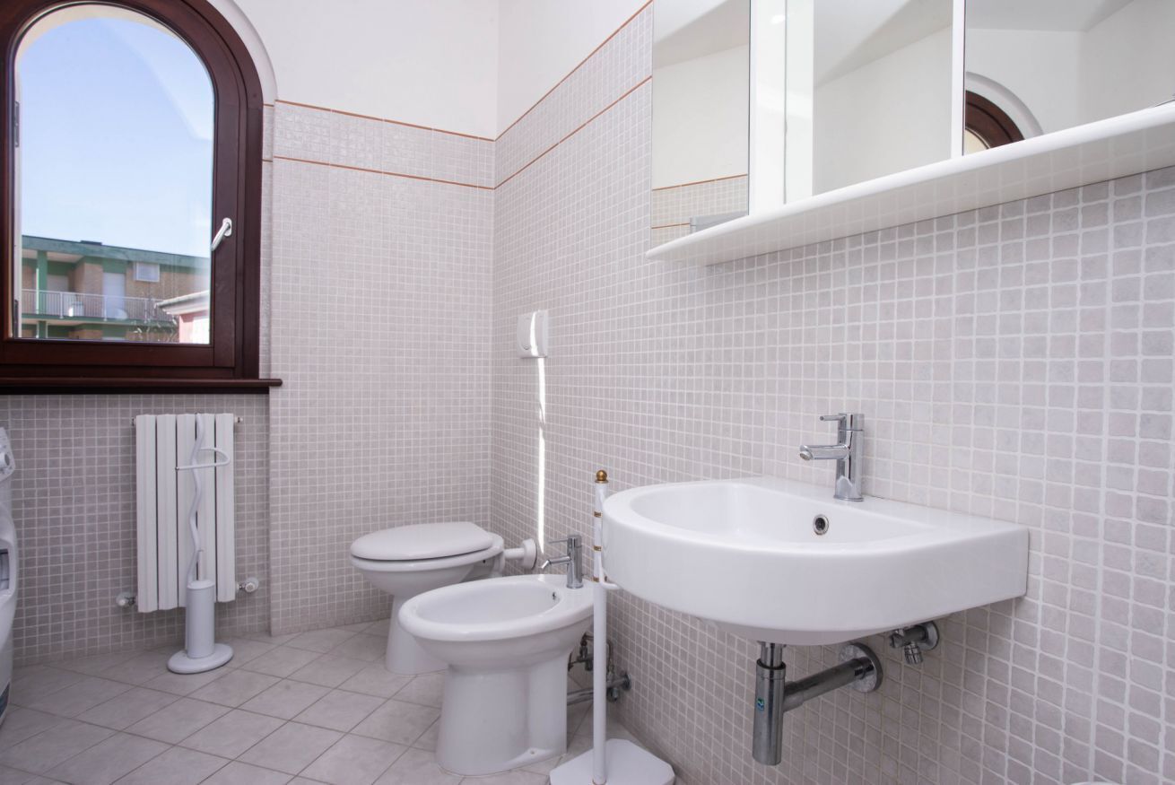 Un bagno moderno con WC, bidet e lavandino, pareti rivestite di piastrelle e una finestra.