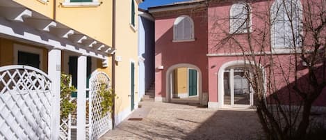 A cobblestone alley between buildings with a white gate, a small staircase, and a tree.
