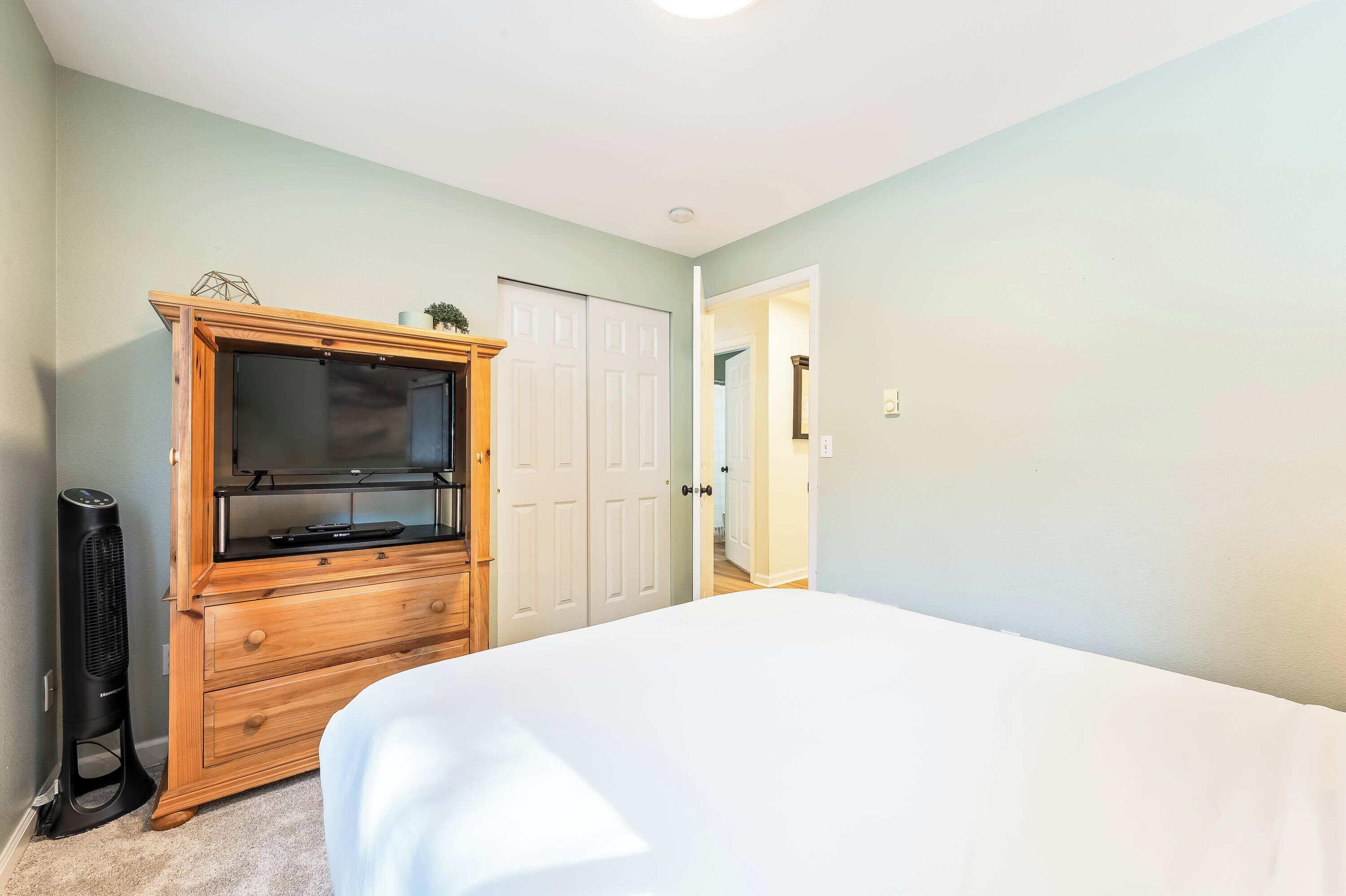 A bedroom with a bed, a wooden dresser, a TV, and a standing heater.