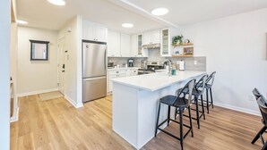 Una cocina moderna con armarios blancos, un refrigerador de acero inoxidable y una isla central con taburetes de bar.