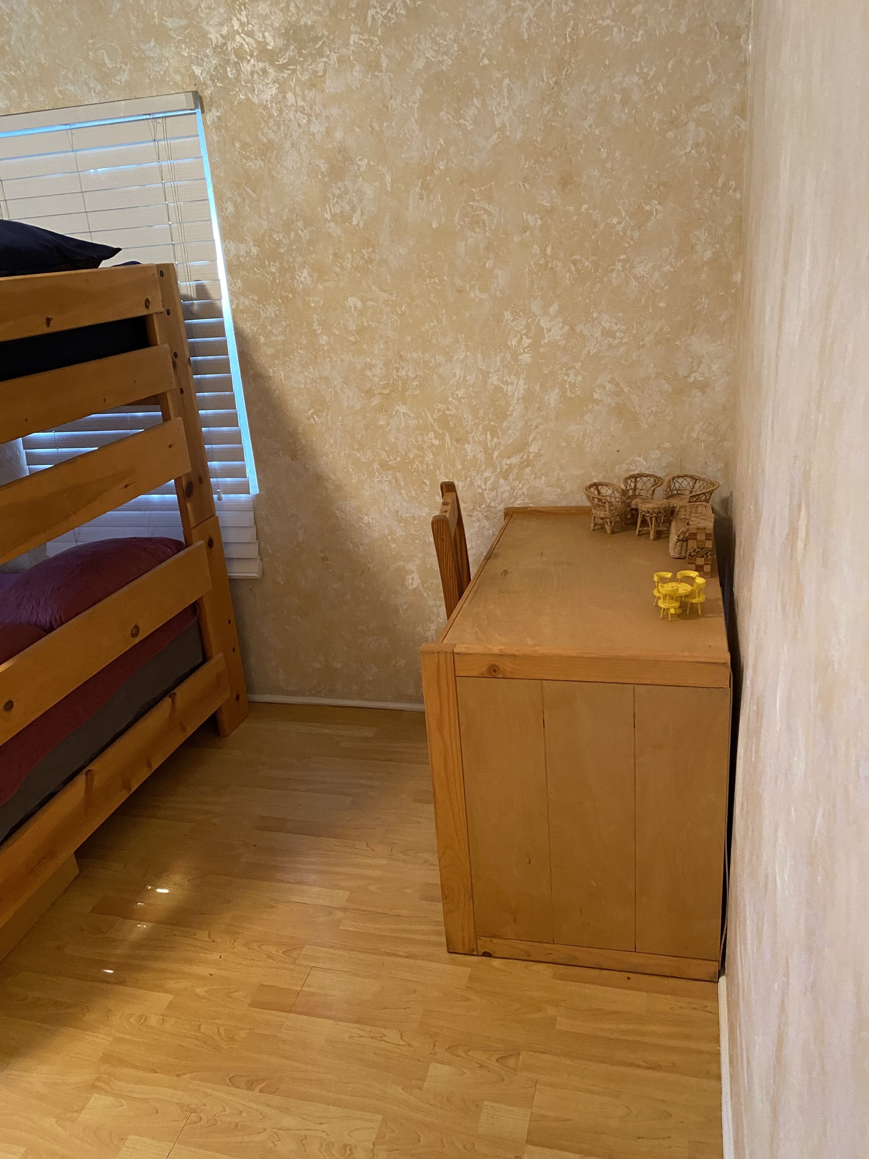 Una cama litera con ventana, una pequeña mesa de madera con sillas y un muro con diseño.