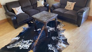 Een woonkamer met twee donkerbruine banken, een klein houten tafeltje en een zwart-wit koeienhuidtapijt.