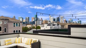 A rooftop terrace with a city skyline view, a wicker sofa, and string lights. - Midtown with a View! (Houston)