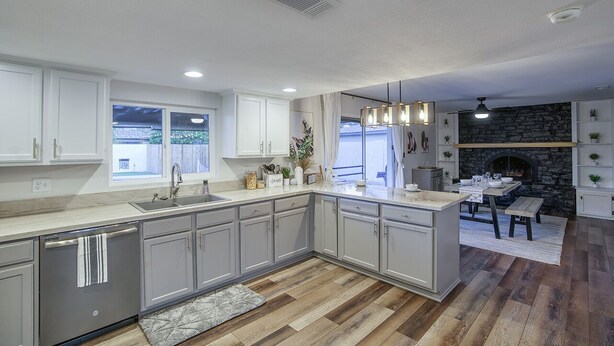 A modern kitchen with grey cabinets, a stone fireplace, and a dining area with a wooden table and benches. - Entertainer’s Retreat: Pool, Hot Tub & Mini Golf! (Mesa)