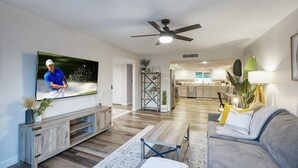 A modern living room with a flat-screen TV, a ceiling fan, and a kitchen in the background. - Entertainer’s Retreat: Pool, Hot Tub & Mini Golf! (Mesa)