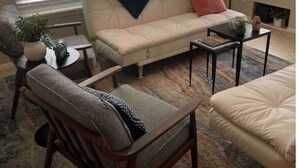 Ett vardagsrum med en beige soffa, två fåtöljer, ett soffbord och en öppen spis.