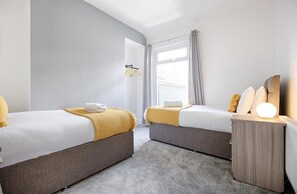 Une chambre d’hôtel avec deux lits, un petit bureau, une lampe et une fenêtre avec des rideaux.