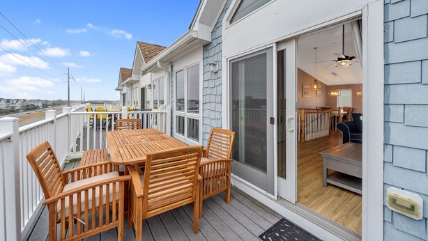 A wooden deck with a table and chairs, a sliding glass door leading to an interior space with a ceiling fan and a dining area.