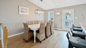 A dining area with a white table and woven chairs, a hanging light fixture, and a door with a view to the outside.