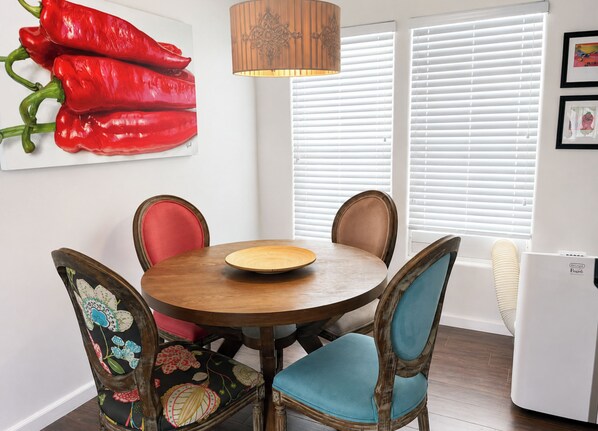 A dining area with a round wooden table, four chairs, a wall-mounted lamp, and a refrigerator.