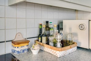A kitchen counter with a woven basket containing various bottles, a salt container, and a small bowl with garlic cloves. - Lovely Terraced 2-bed House Near Hinksey Park (Oxford)