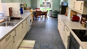 A kitchen with a central island, a built-in washing machine, a red toaster, and a dining area with a table and chairs. - Lovely Terraced 2-bed House Near Hinksey Park (Oxford)