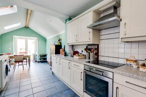 A kitchen with white cabinets, a built-in oven, and a dining area with a table and chairs. - Lovely Terraced 2-bed House Near Hinksey Park (Oxford)