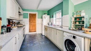 A compact kitchen with white cabinets, a washing machine, and a wooden door. - Lovely Terraced 2-bed House Near Hinksey Park (Oxford)