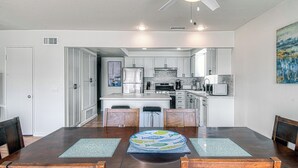 Une cuisine moderne avec des meubles blancs, un îlot central et un coin repas comprenant une table et des chaises en bois.