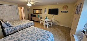 A room with two beds, a small table with chairs, a TV, and a ceiling fan.