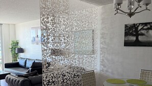 A modern living room with a sectional sofa, a dining table with chairs, and a decorative partition with a floral pattern.