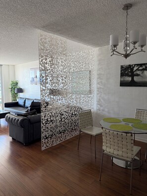 Un salon moderne comprenant un canapé d’angle, une table à manger avec des chaises et un élément de séparation décoratif orné d’un motif floral.