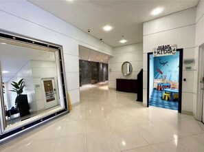 Un hall d’hôtel doté d’un grand miroir, d’un comptoir d’accueil et d’un espace de jeux pour enfants intitulé « Ocean Reserve Kids ».