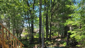 A wooden deck leading to a covered area, surrounded by a forested area with two kayaks on the ground.