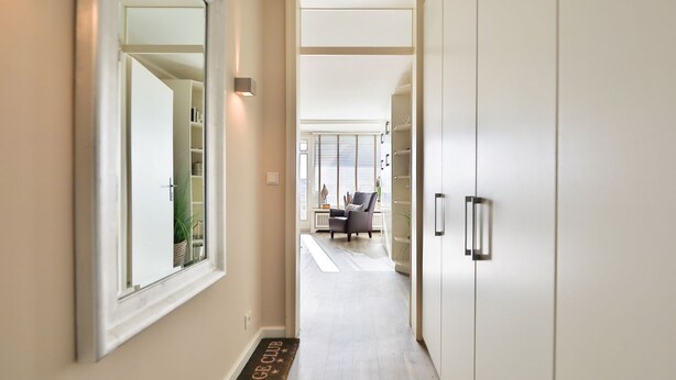 A hallway with a mirrored wall, a door with a handle, and a doormat with text.