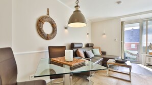 A modern living room with a glass coffee table, leather sofa, and a hanging light fixture.