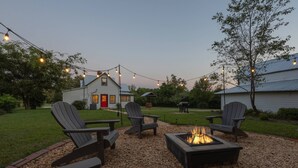 Un patio con sillas Adirondack y un brasero, rodeado de grava y luces colgantes.