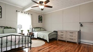 Un dormitorio con dos camas, un ventilador de techo, un aparador y una ventana con cortinas.