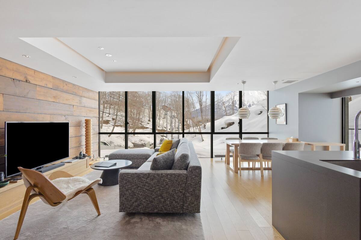 A modern living room with a large TV, a sofa, a wooden chair, and a dining area with a table and chairs.