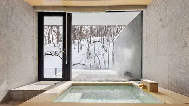 A modern spa with a glass-enclosed hot tub, a view of a snowy forest, and a minimalist design.