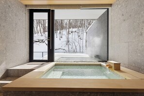 Un moderno spa con un jacuzzi de paredes de vidrio, vista a un bosque nevado y un diseño minimalista.