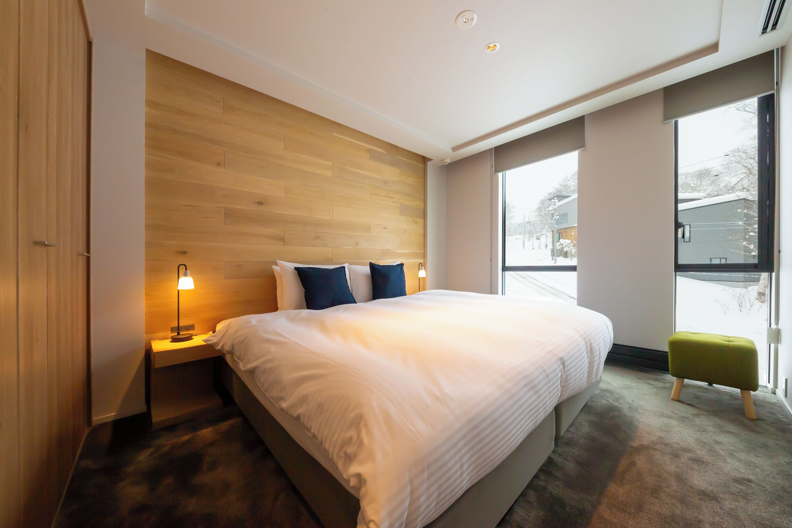 Una habitación de hotel moderna con una cama grande, cabecera de madera, lámparas de noche y vistas al exterior.