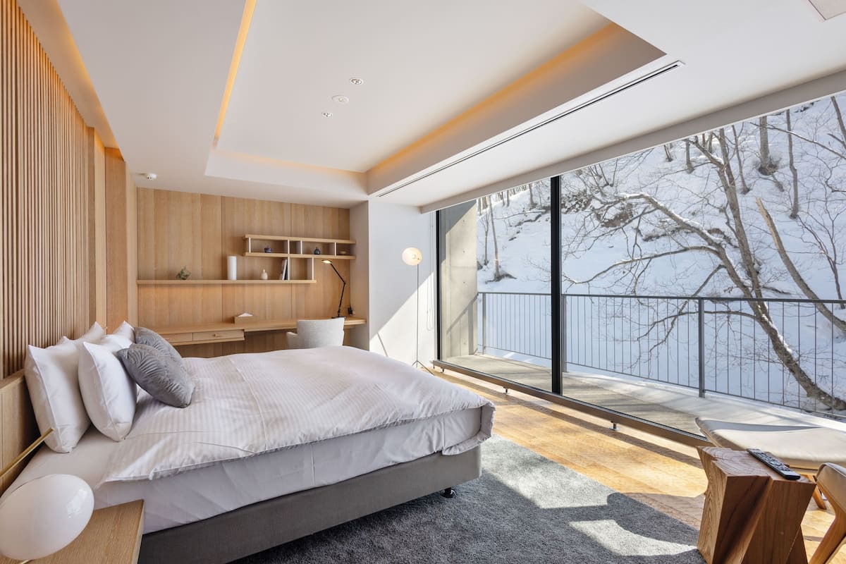 A modern bedroom with a large bed, built-in shelving, a desk, and a view of a snowy landscape through a large window.
