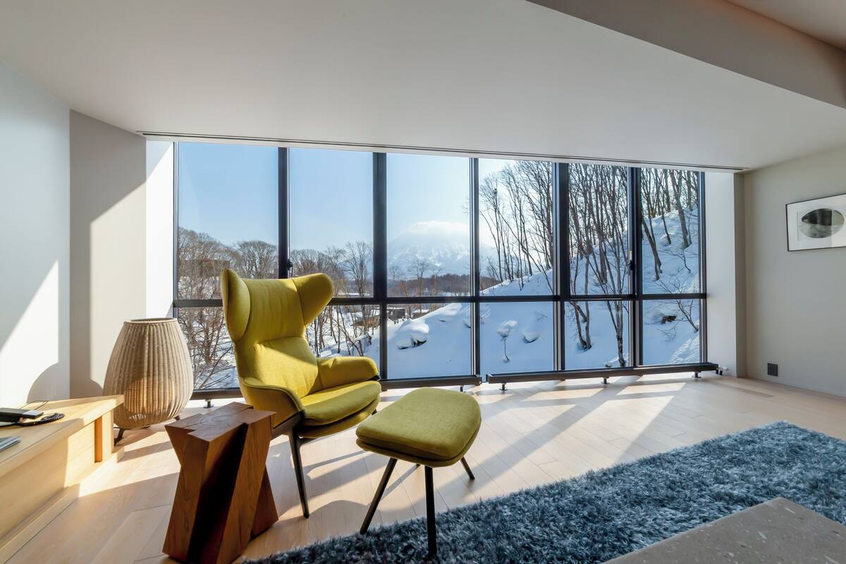 A modern room with a large window, a yellow armchair, a wooden coffee table, and a blue rug.