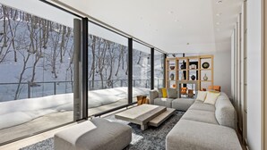 A modern living room with a large window, a gray sectional sofa, a coffee table, and a bookshelf.