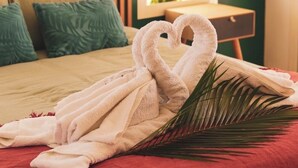 Una cama bien hecha con dos toallas formando cisnes, una colcha roja y una hoja de palma sobre la cama.