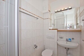 A bathroom with a shower, toilet, sink, and a mirror with lights. - Close to the beach, balcony, free AHOI adventure pool - Strandresidenz Brandenburg FeWo 07 (Göhren)